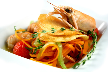 Braised royal shrimps with vegetables and potato chips on white plateの写真素材