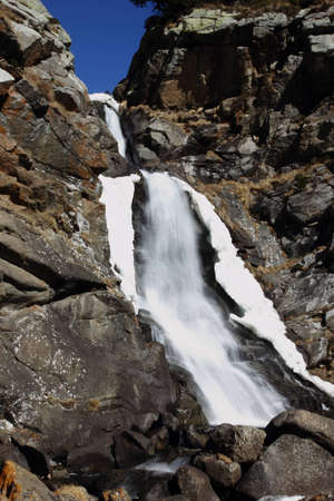 Spring waterfall between snow and stonesの写真素材