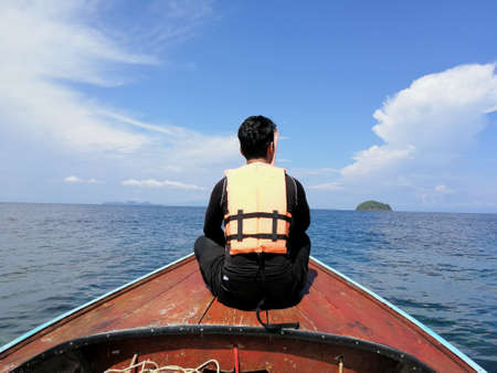 Asian man wearing orange color life jacket on a tail boat during the dayの写真素材