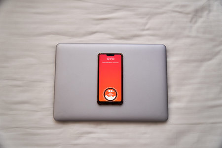 Oyo hotel chain logo displayed in mobile phone on bed with a laptop