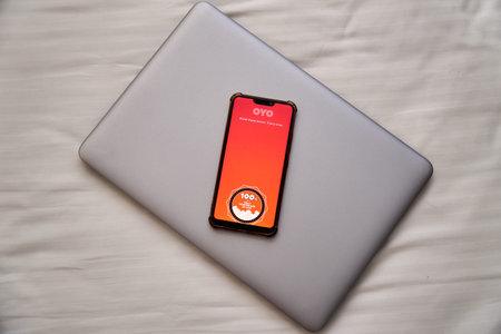 Oyo hotel chain logo displayed in mobile phone on bed with a laptop