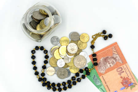 Top view of coins, Malaysia Ringgit bank notes and rosary over white backgroundの写真素材