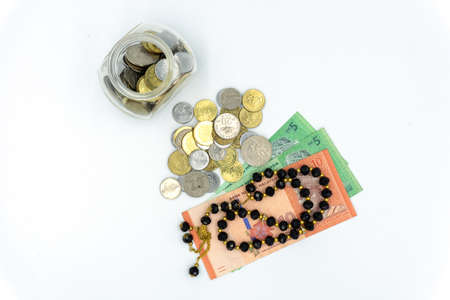 Top view of coins, Malaysia Ringgit bank notes and rosary over white backgroundの写真素材