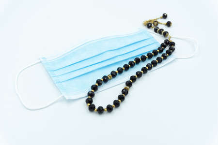 Surgical face mask and black prayer beads over white backgroundの写真素材