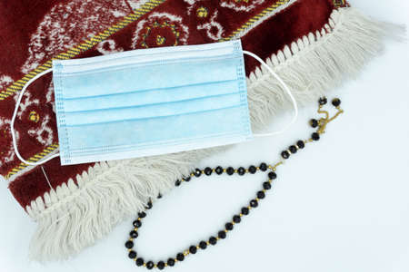 Face mask, black prayer beads with red prayer mat over white backgroundの写真素材
