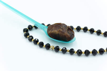 Dates on a blue spoon with black prayer beads over white background