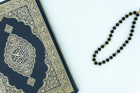 Quran and black colored prayer beads over white background