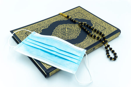 Surgical face mask, Quran and black prayer beads over white background