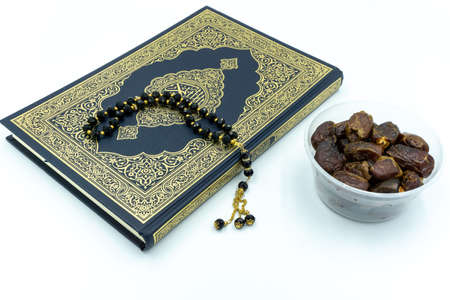 Quran with black colored prayer beads and dates in a plastic container over white backgroundの写真素材