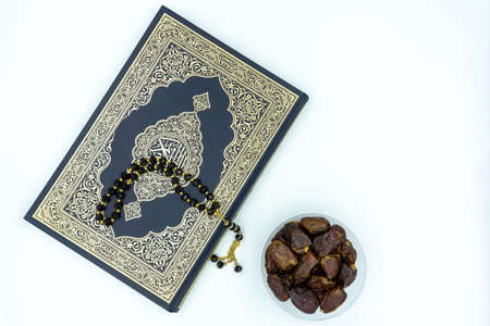 Quran and black prayer beads and dates in plastic container over white backgroundの写真素材