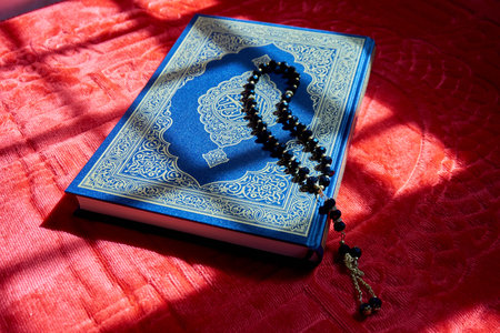 Prayer beads on the Quran over red prayer mat with sunlight