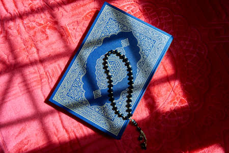 Prayer beads on the Quran over red prayer mat with sunlightの写真素材