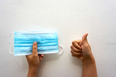 Hand holding surgical face mask with thumbs up gesture over white backgroundの写真素材