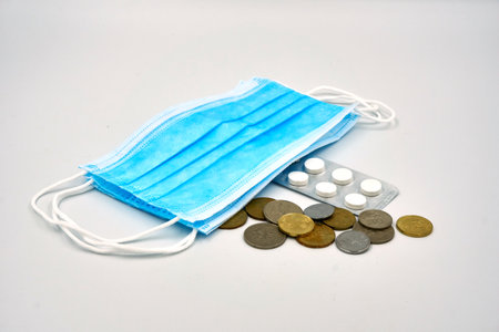 Blue surgical face mask, Ringgit coin and medicine pills over white backgroundの写真素材