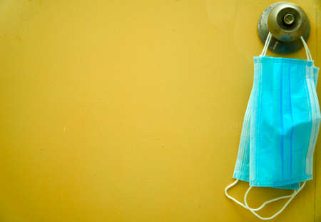 Two blue surgical face mask hanging at the door knob over yellow backgroundの写真素材