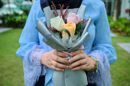 Selective focus of muslim women wearing blue dress holding bouquet of rosesの写真素材