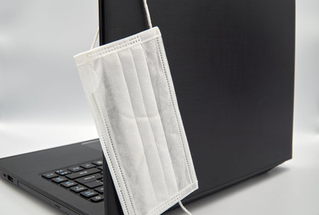 White surgical face mask hanging on top of laptop