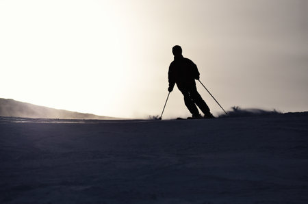 silhouette of alpine skier going down the ski slope in contrasting lightの写真素材