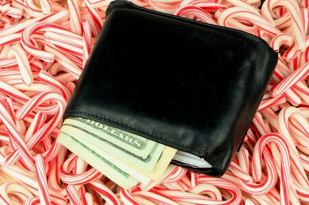 Illustrating the high cost of the Christmas holidays, a wallet full of money lies on a bed of candy canes.の写真素材