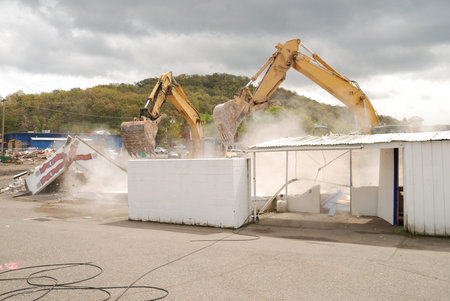 Large track hoe excavator demolishing a concrete block building making way for new commercial retail businessのeditorial素材