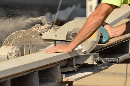 Carpenter uses a compound electric cut off saw to cut trim boards for a new commercial residential projectの写真素材