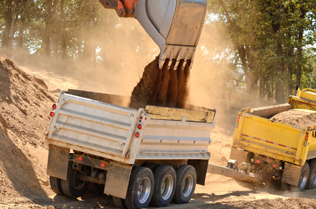Large track hoe excavator filling a dump truck with rock and soil for fill for a new commercial development road construction projectの写真素材