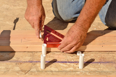 Building contractor worker using a drill for holes for plumbing stubouts in the base plate of the...