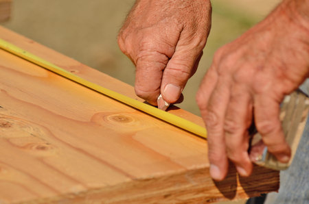 Building contractor worker measuring for cuts on the joist rim board on a new home construciton...
