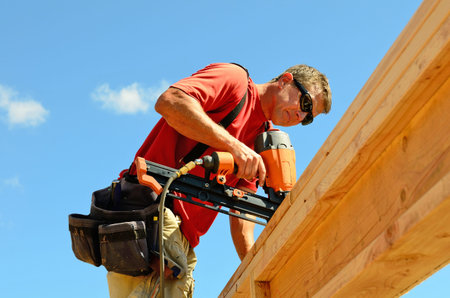 Building contractor worker with a air nail gun  nailer working on the corner of the top plate of the...