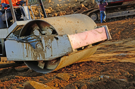 Road roller compactor compressing soil and rock on a new commercial road construction project
