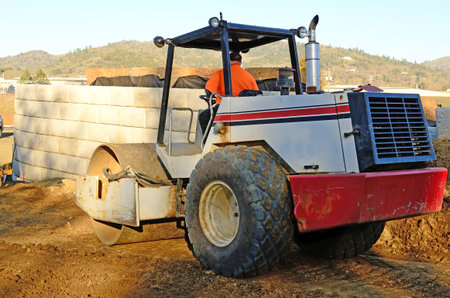 Road roller compactor compressing soil and rock on a new commercial road construction project