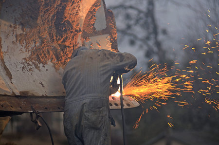 A mechanic welder uses a plasma cutter to cut metal plates from the blade of a bulldozer on a...