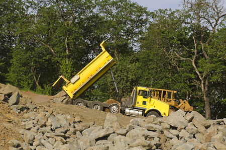 Dump truck at a new commercial construction development project dumping a load of large rock for new roadの写真素材