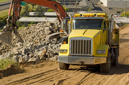 A large track hoe excavator loads a dump truck with dirt and rock on a new commercial construction...