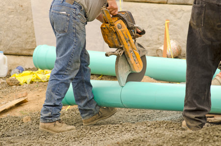 Construction workers using power saw equipment install water pipe utilities at a new commercial ...