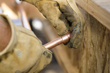 Plumbing contractor works sweating the joints on the copper pipe domestic water system on a luxury custom homeの写真素材