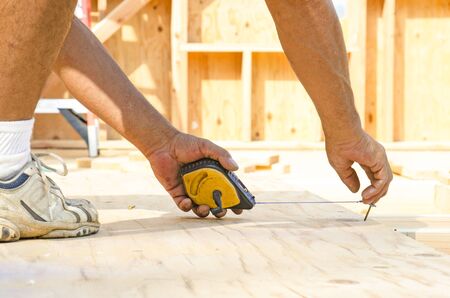 Framing contractor measuring and  chalk line to install plywood sub siding to wood joistの写真素材