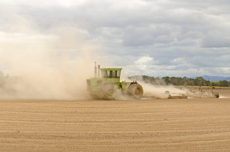 Large agricultural tractor pulling a steel disc harrow to prep the soil for planting with fall storm...
