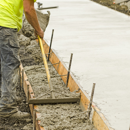 Concrete construction contractor installing a sidewalk, curb and storm drainage gutter on a new urban road street projectの写真素材