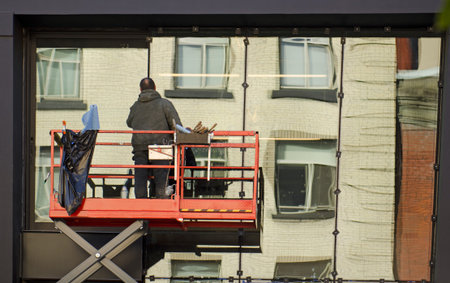 Construction window contractor installing new windows in a downtown city building using a man liftの写真素材