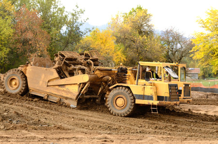 Large box scraper tractor works at moving soil and rock for a new commercial housing development.