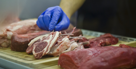 Hand with glove taking a Lamb cutlet from a showcase with meatの写真素材