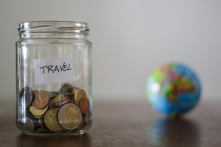 Travel money savings in a glass jar with earth globe on the backgroundの写真素材