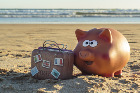 Piggy bank and travel luggage on beachの写真素材