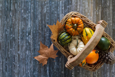 Top view of pumpkins in wicker basket and dry leaves on blue backgroundの写真素材