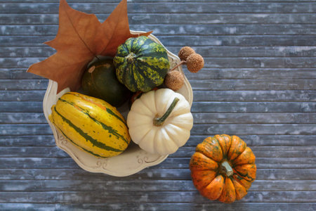 Top view of bowl with pumpkins and autumnal leaves on blue background