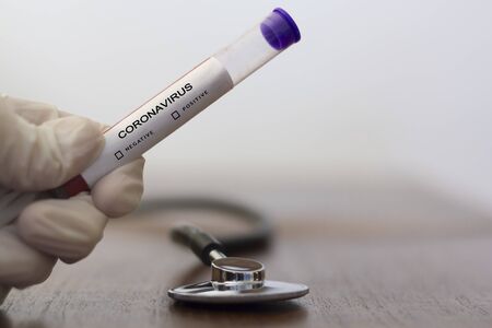 Hand with glove holding Coronavirus blood test, with medical stethoscope on the tableの写真素材
