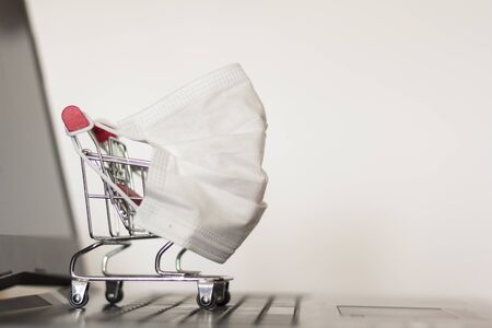 Shopping cart with protective face mask on laptop computer. Online shopping in isolation or quarantine, Coronavirus Covid-19 pandemicの写真素材