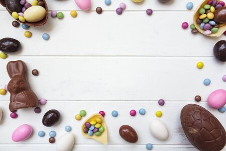Easter background with chocolate eggs, easter bunny and other sweets on white wooden table with copy spaceの写真素材
