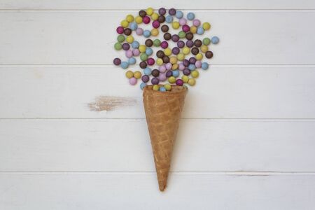 Top view of ice cream cone with sweet colorful candies on white wooden tableの写真素材
